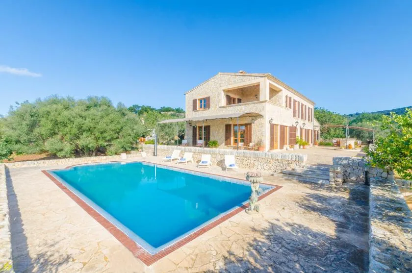 Una piscina está junto a una casa de piedra clara y un patio pavimentado.