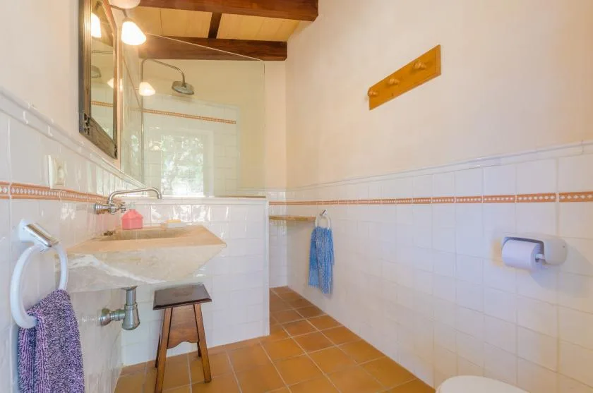 Un baño con azulejos, lavabo, ducha y vigas de madera en el techo.