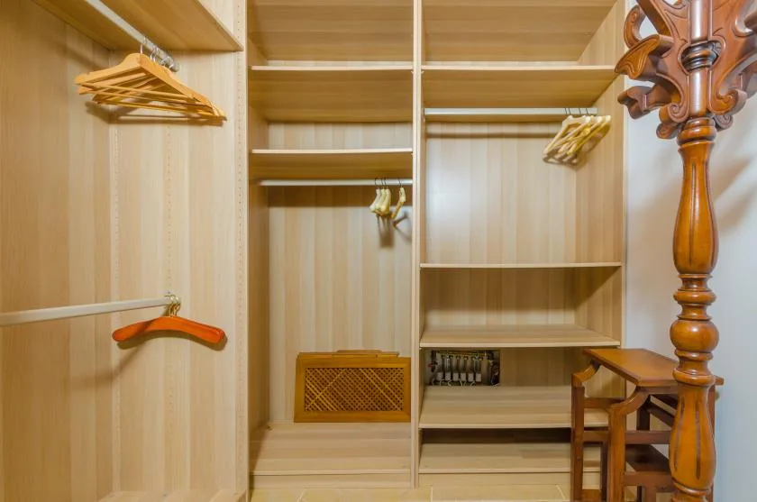 Un vestidor de madera con estantes abiertos, barras para colgar y varias perchas.