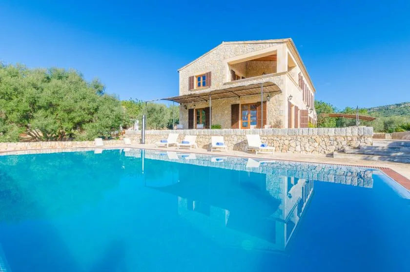 Una casa de piedra está junto a una piscina, con tumbonas a lo largo del borde.