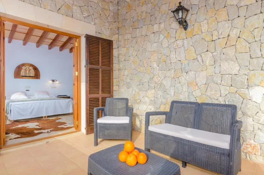 Un patio con paredes de piedra, asientos de mimbre y una mesa con naranjas.