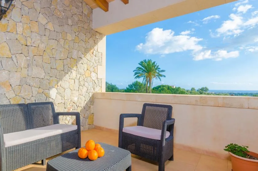 Una zona de estar exterior cubierta da a una palmera y un paisaje verde.