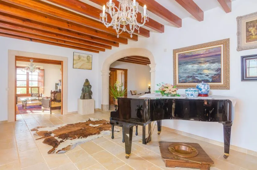 Una luminosa sala de estar tiene un piano de cola negro bajo vigas de madera expuestas.