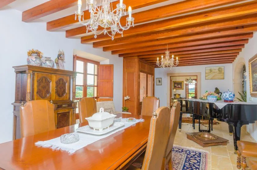 Un comedor formal con una mesa larga, vigas de madera en el techo y un piano.