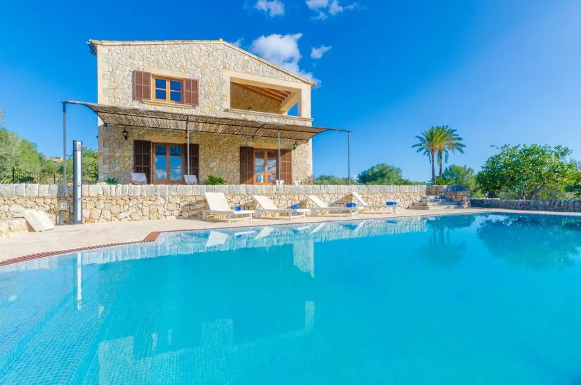 Una piscina frente a una casa de piedra, con asientos para descansar junto al borde.