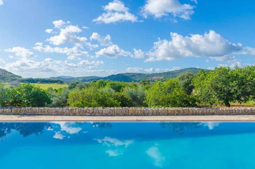 Una piscina al aire libre tiene vistas a colinas verdes bajo un cielo parcialmente nublado.