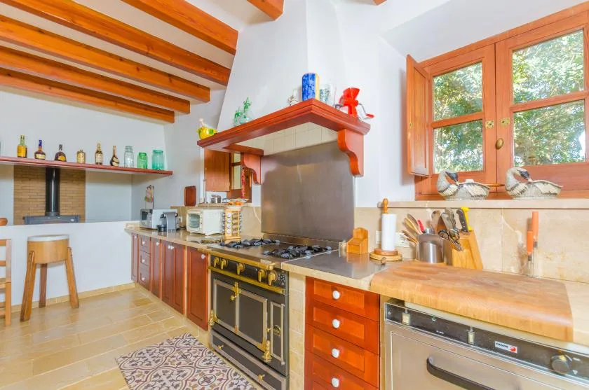 Una cocina luminosa con gabinetes de madera, una estufa grande y ventanas con vista a la vegetación.