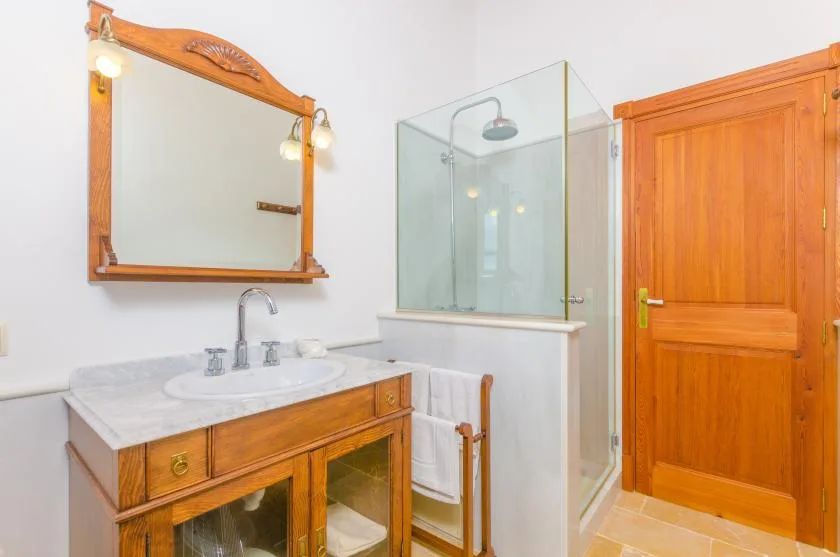 Un tocador y un espejo de baño están junto a una ducha de vidrio y una puerta de madera.