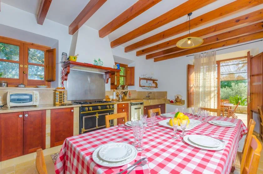 Comedor con mantel de cuadros rojos y blancos y una cocina al fondo.