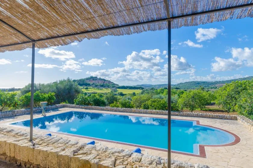 Una piscina al aire libre está bajo un toldo de caña, con vistas a colinas verdes.