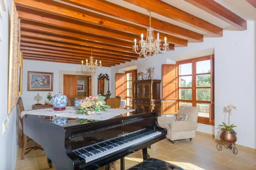 Un salón luminoso con un piano de cola, asientos y vigas de madera vistas.