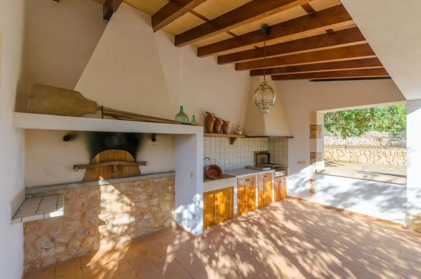 Una cocina rústica con horno de piedra, encimera de azulejos y vigas de madera a la vista.