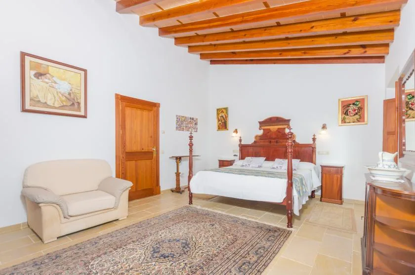 Un dormitorio con una cama de madera, un sillón claro y vigas de techo vistas.