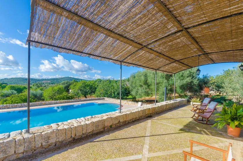 Una terraza sombreada junto a la piscina mira hacia colinas verdes, con asientos junto al agua.