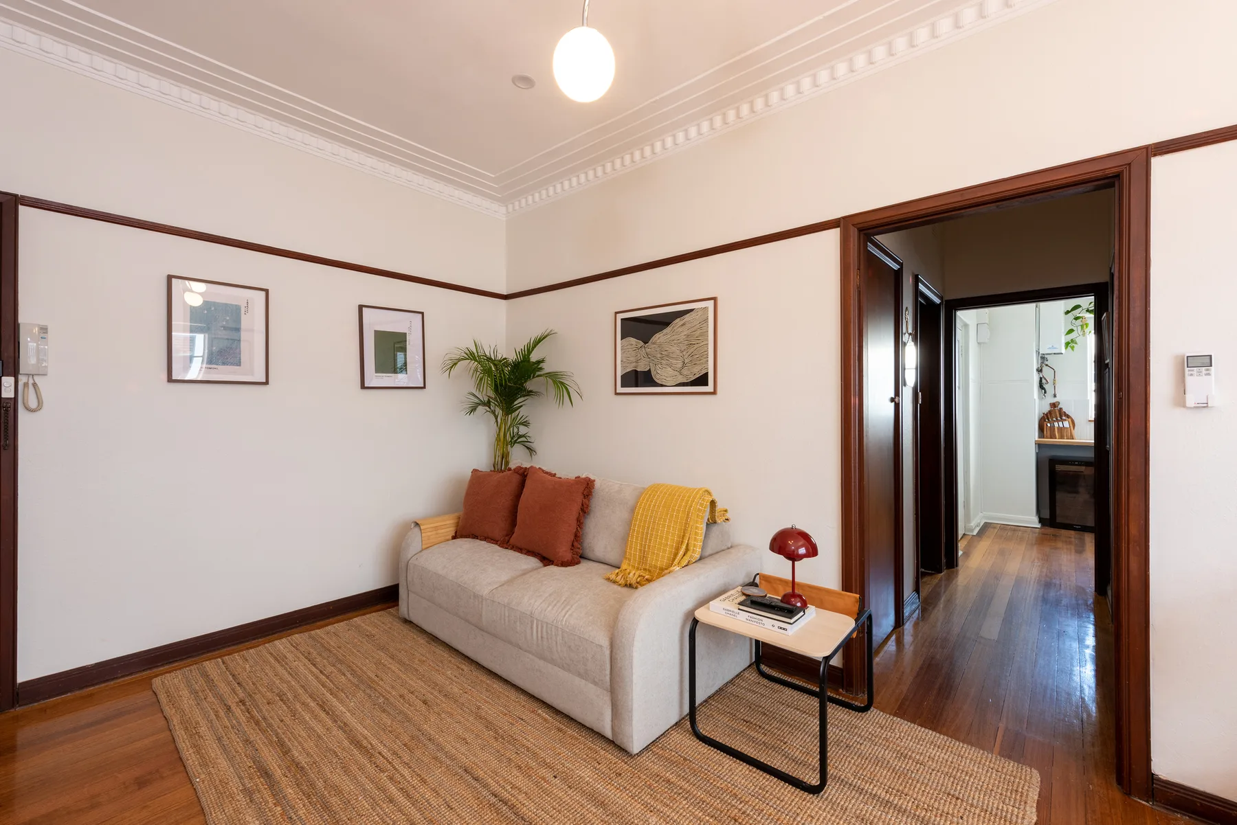 A sitting area with a light-colored couch, framed artwork, and a woven rug.