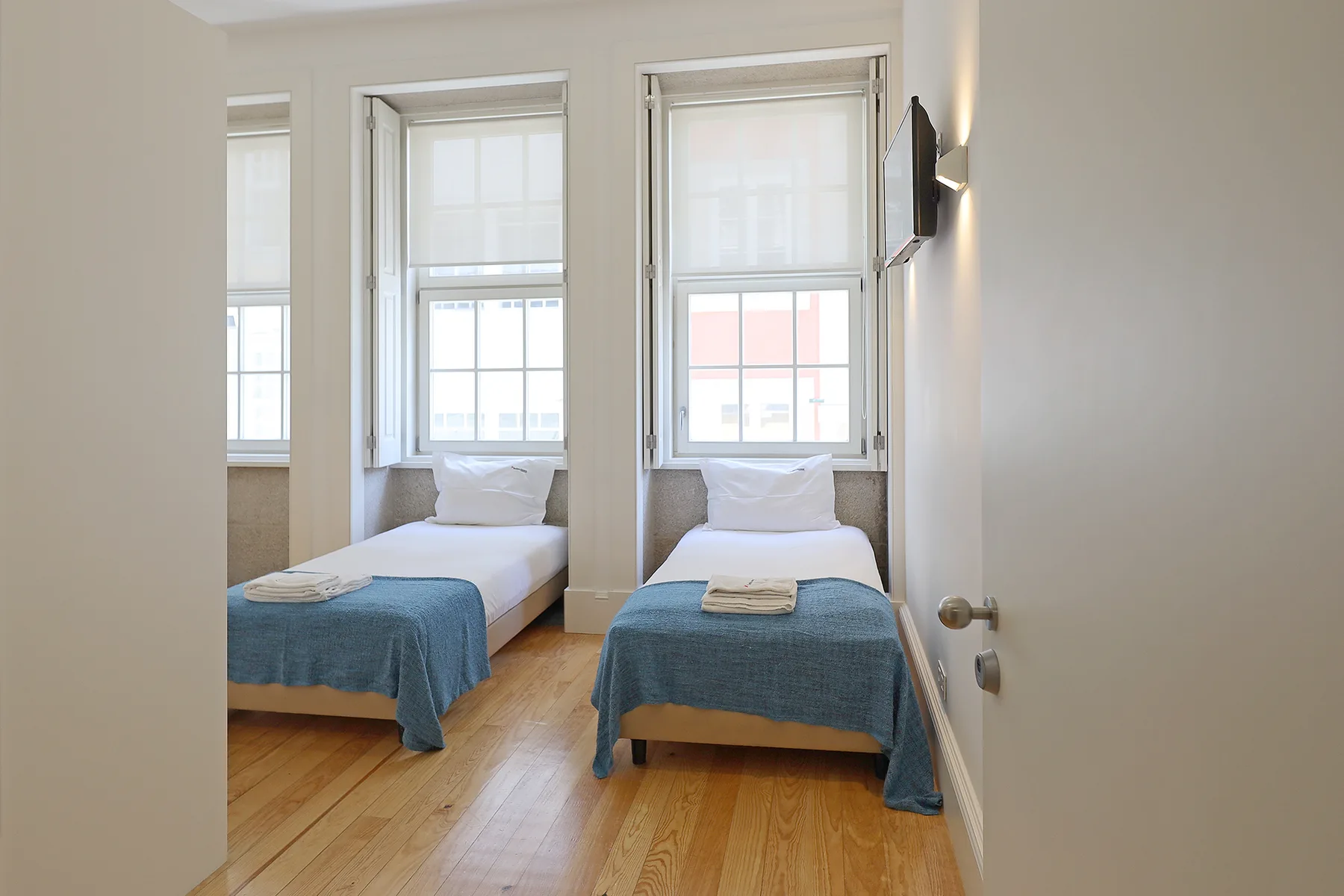A bedroom with two single beds beneath bright windows.