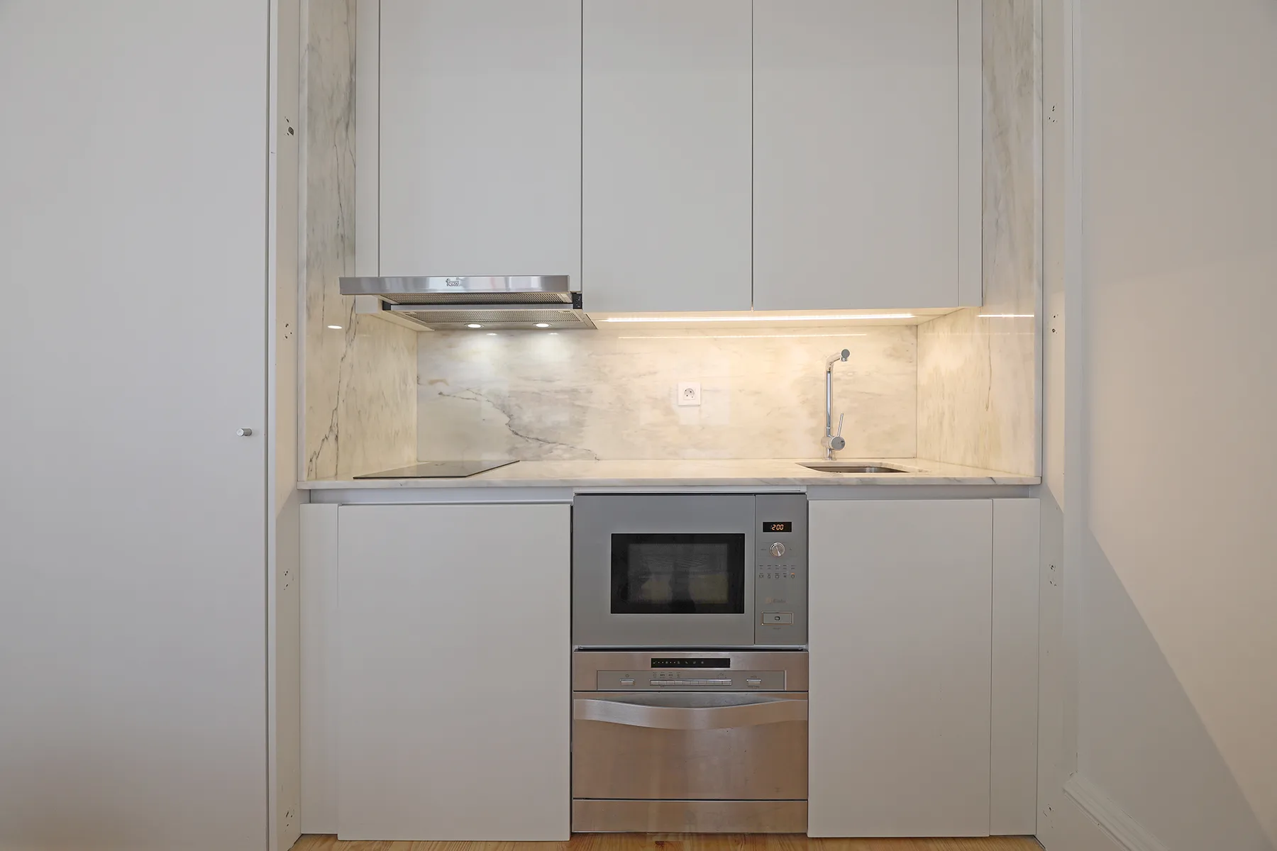 A compact kitchen with pale cabinets, a countertop, and built-in appliances.