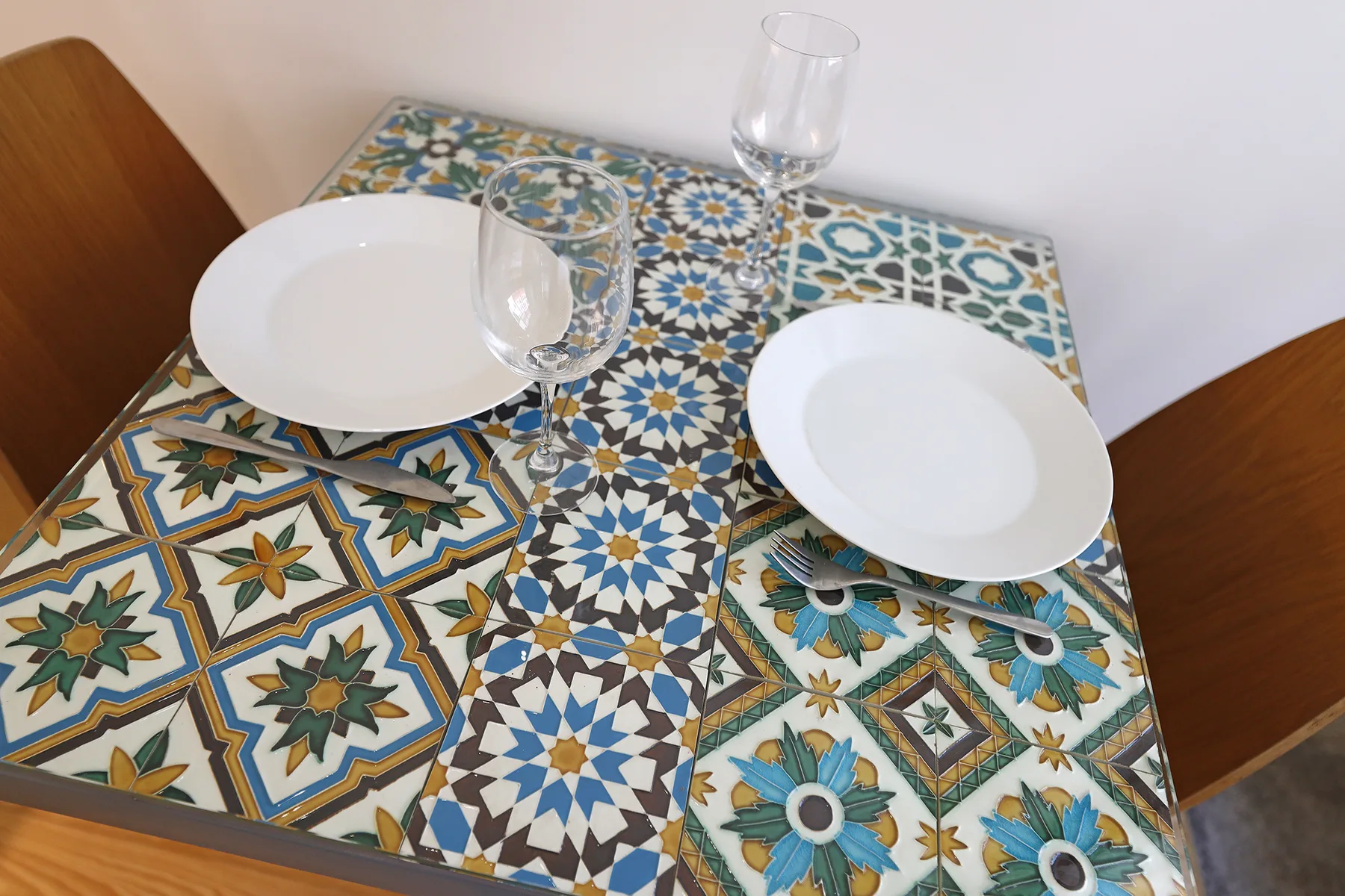 A dining table with two plates and clear glasses on a colorful patterned surface.