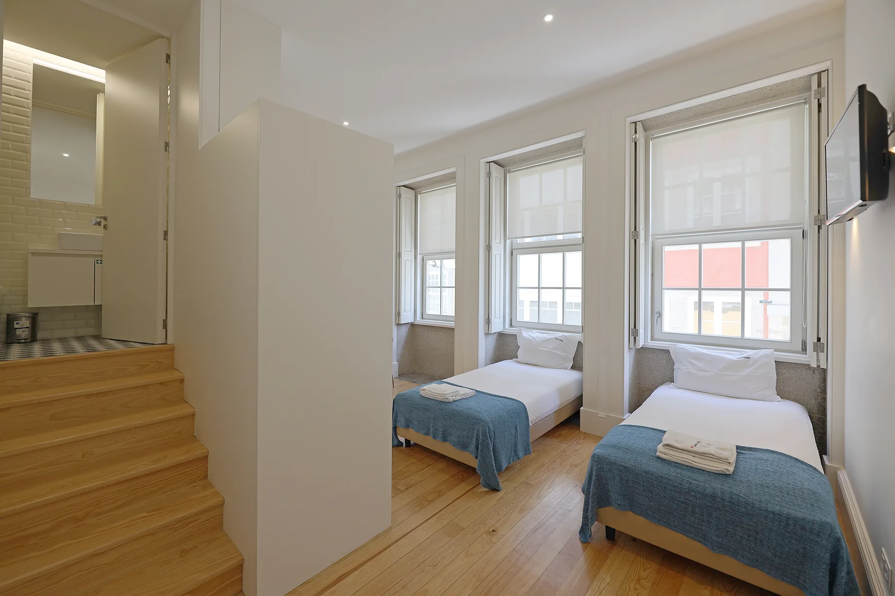 A bedroom with two single beds beneath large windows.