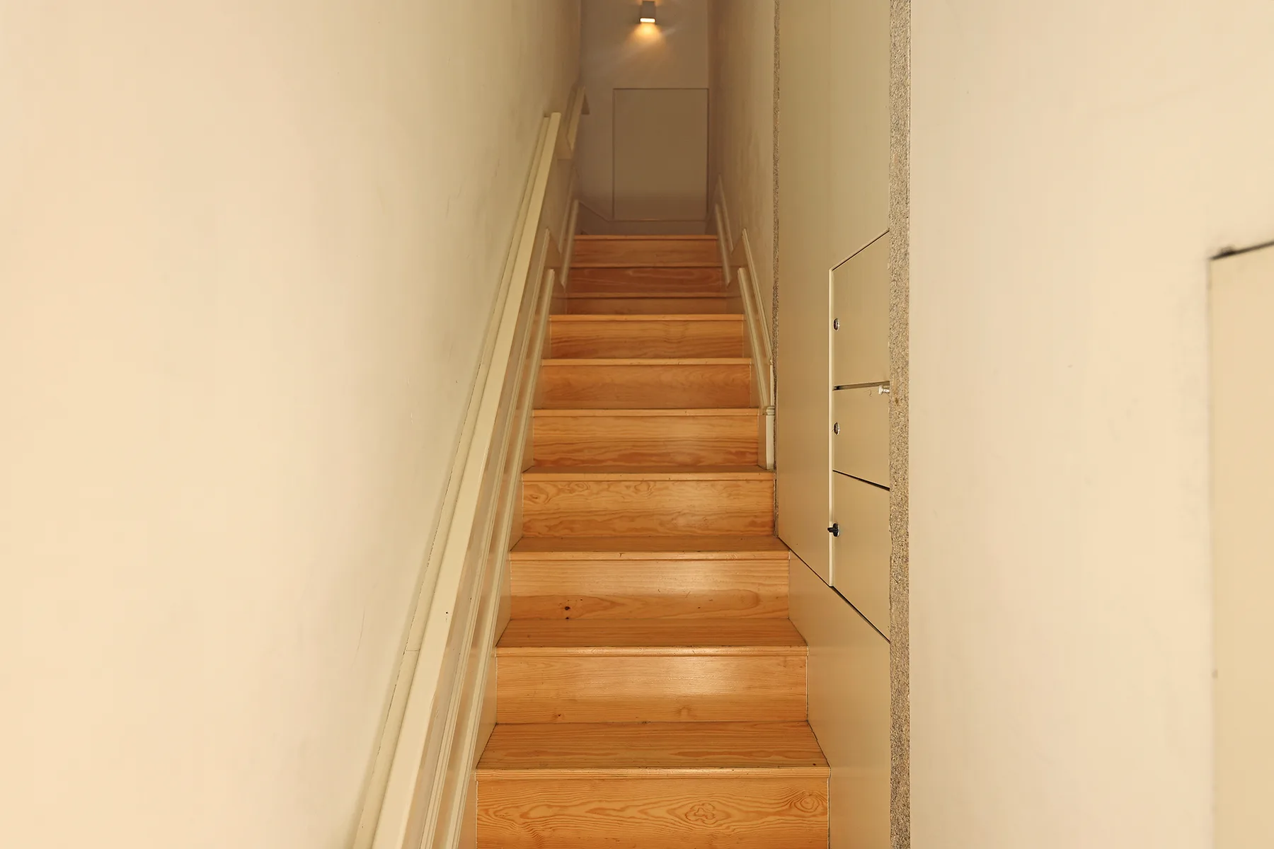 A narrow indoor staircase with wooden steps and light-colored walls.