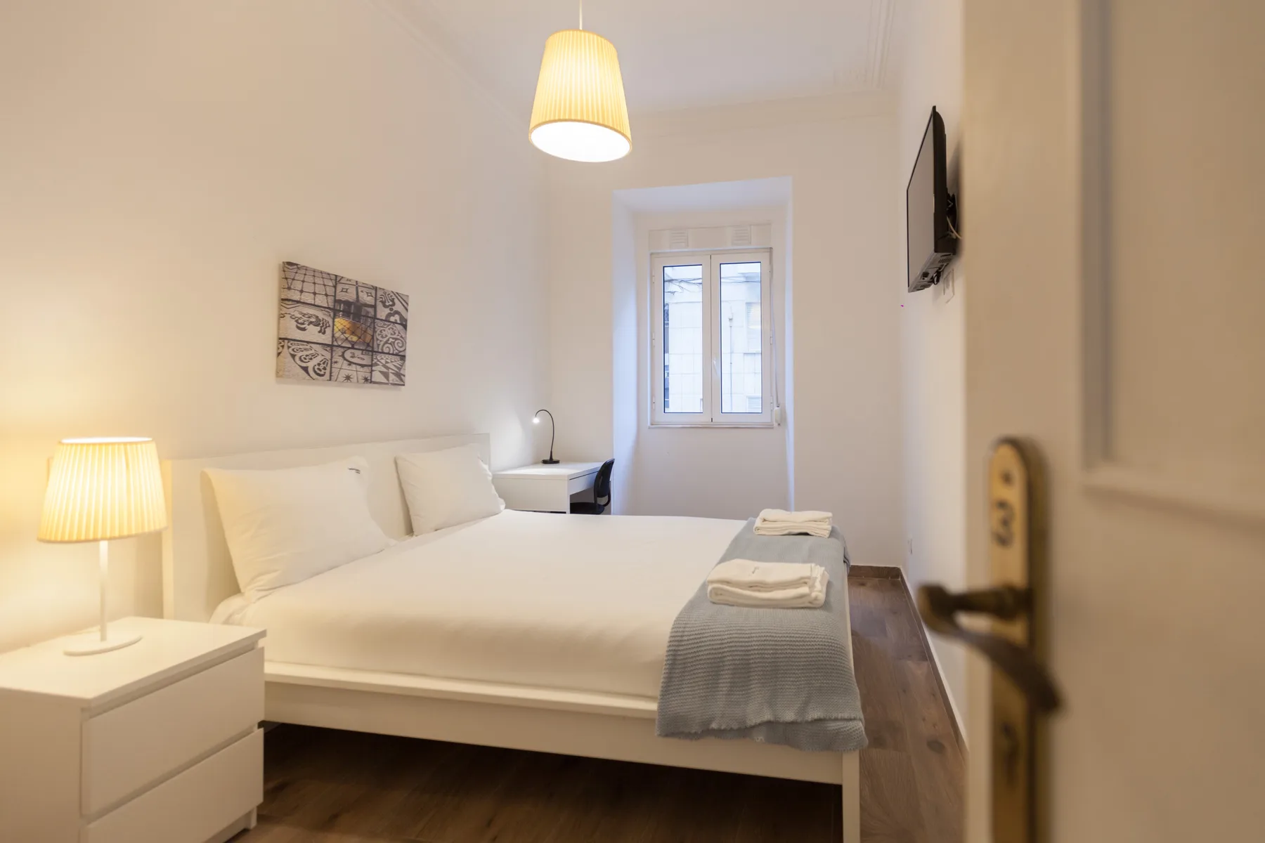 Un dormitorio luminoso con una cama tendida, lámparas de mesilla y una ventana.
