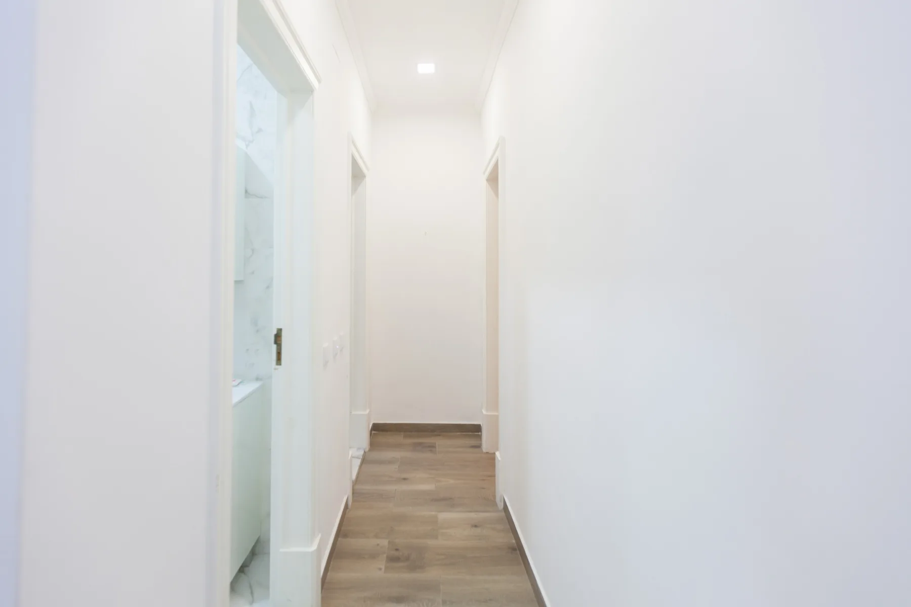 Un pasillo luminoso con suelo de aspecto madera clara y varias puertas.