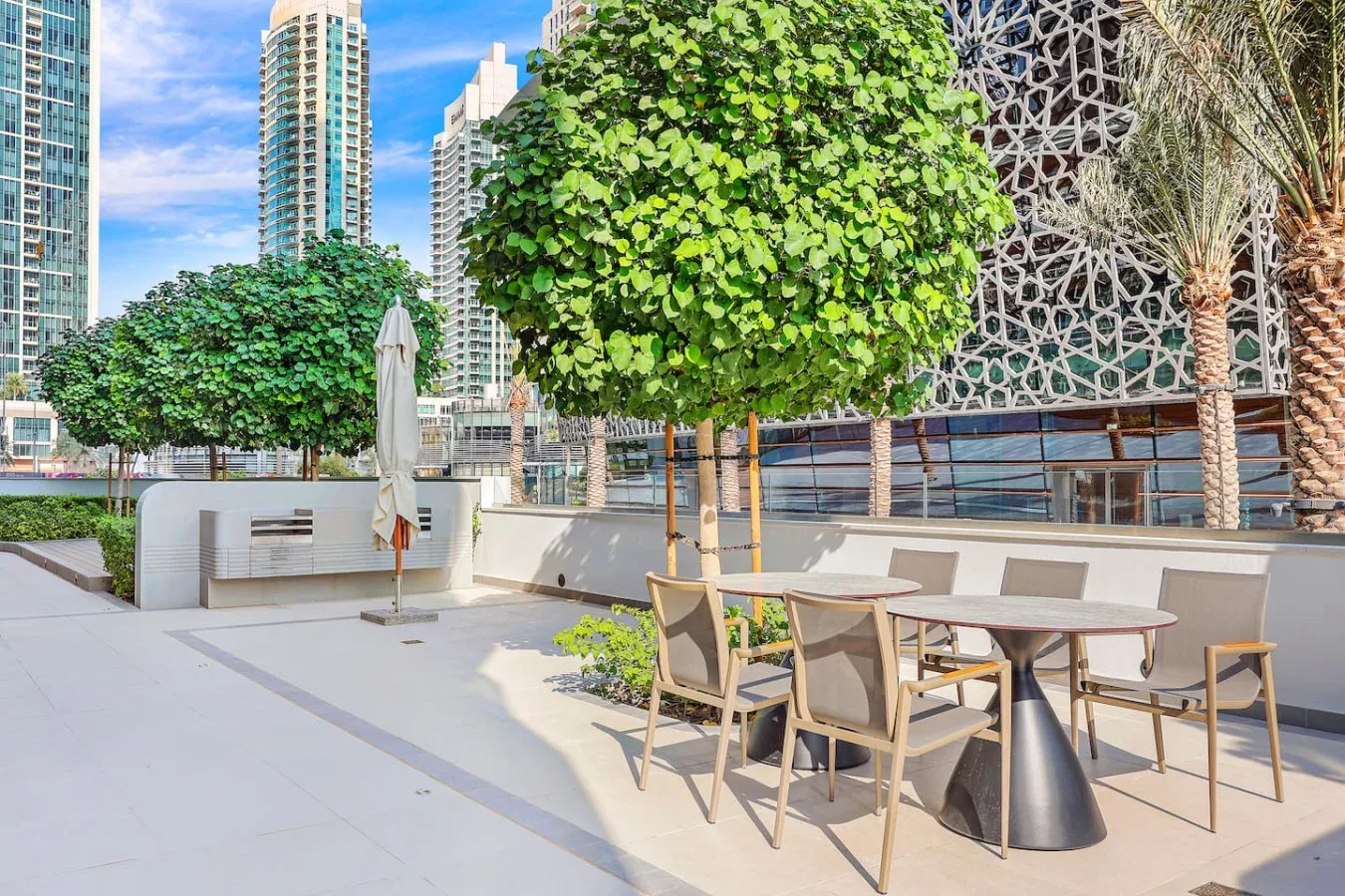 Una zona de comedor al aire libre con mesas y asientos bajo árboles frondosos.