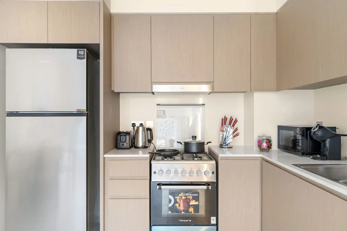 Una cocina compacta con gabinetes claros, refrigerador y estufa.