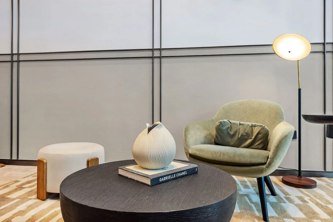 Una zona de estar moderna con una mesa redonda, un sillón tapizado y una lámpara de pie.