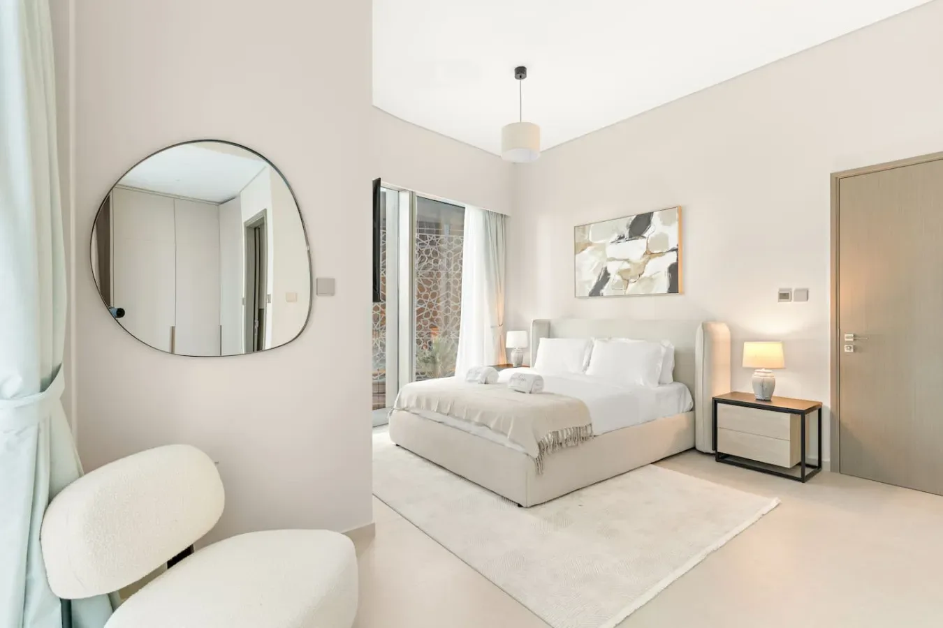 A bright bedroom with a bed, bedside table, and round wall mirror.