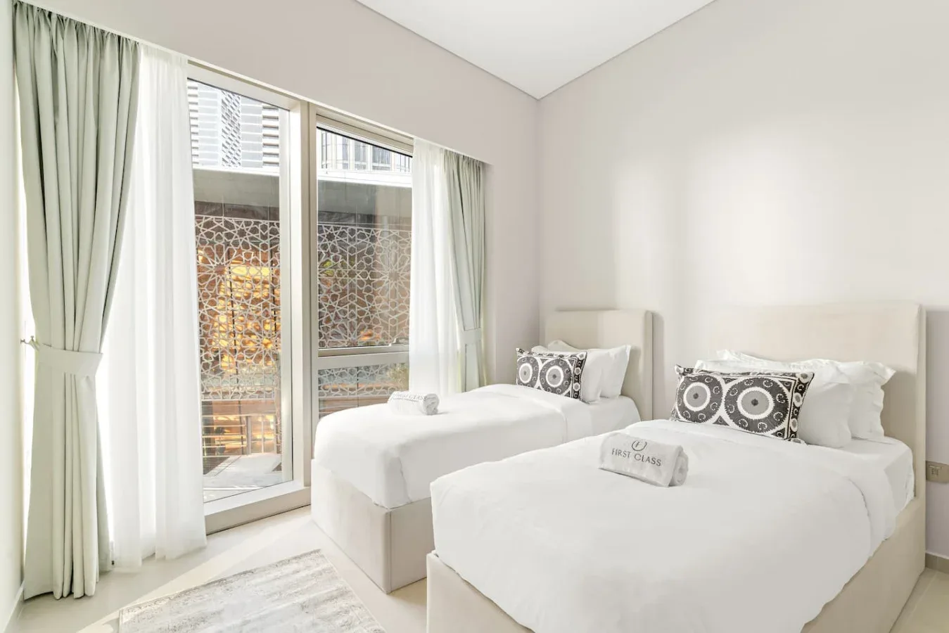 Un dormitorio luminoso con dos camas junto a grandes ventanas con cortinas.