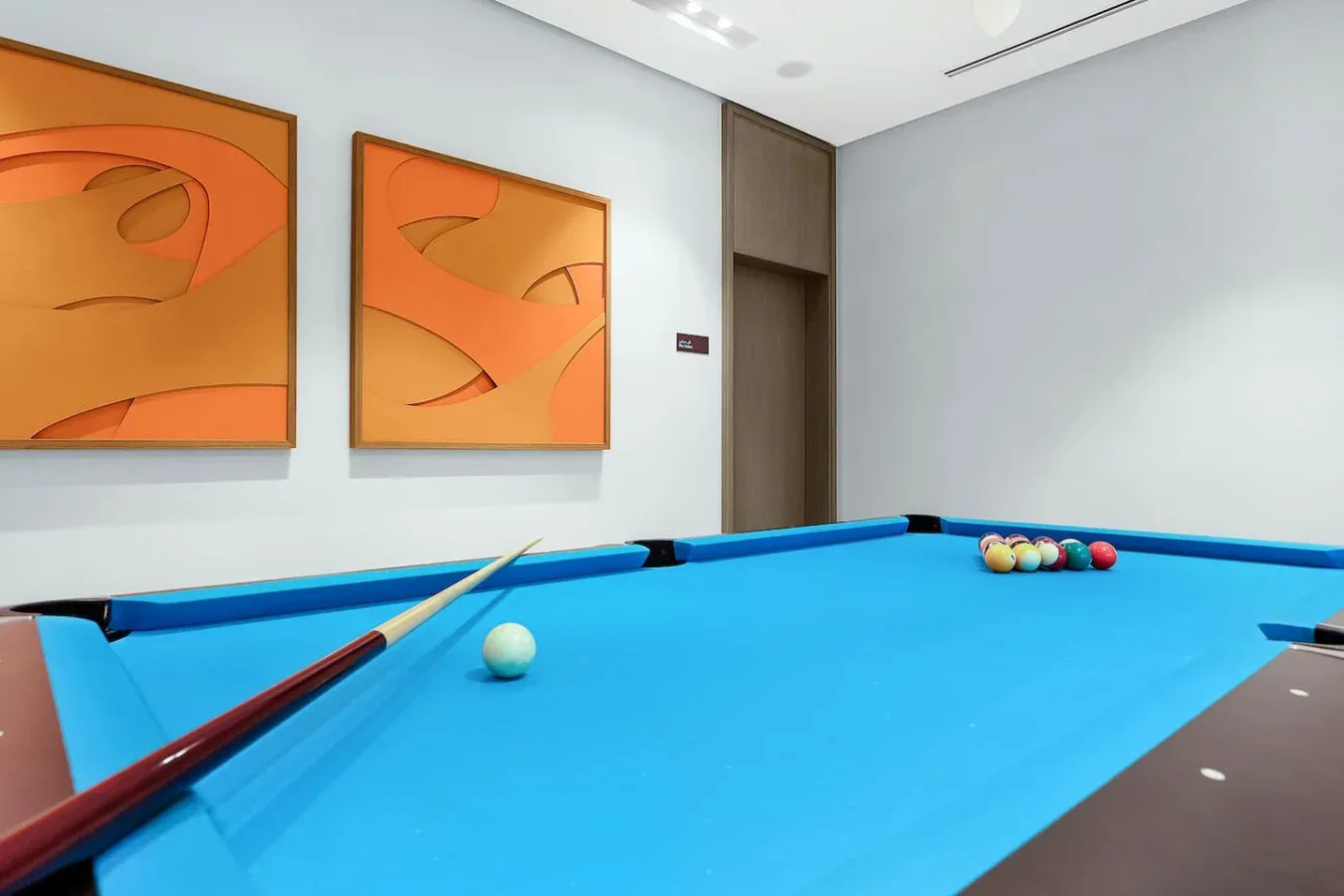 Una sala de billar con una mesa azul y arte abstracto naranja en la pared.
