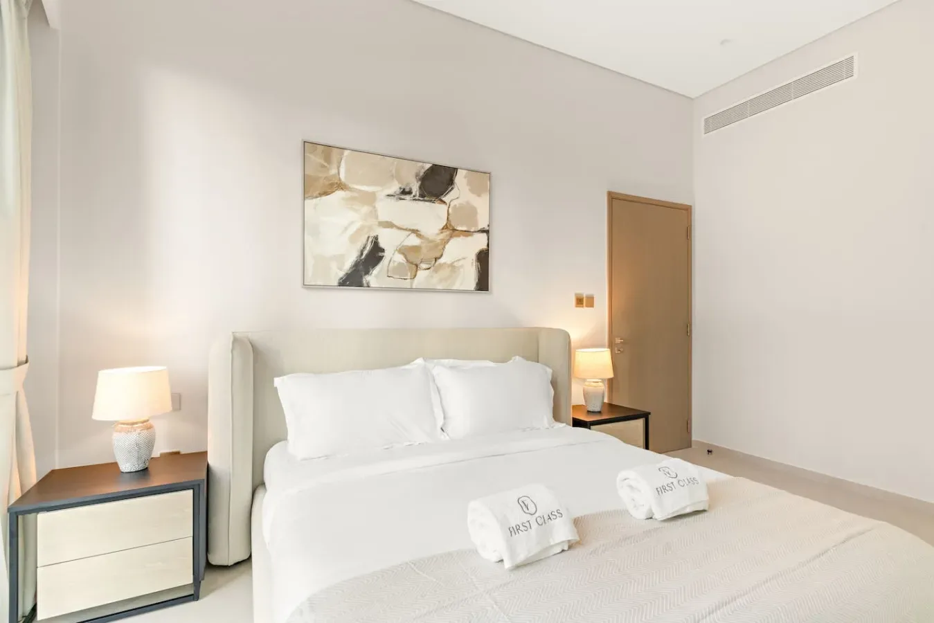 Un dormitorio luminoso con una cama tendida y una obra abstracta sobre el cabecero.