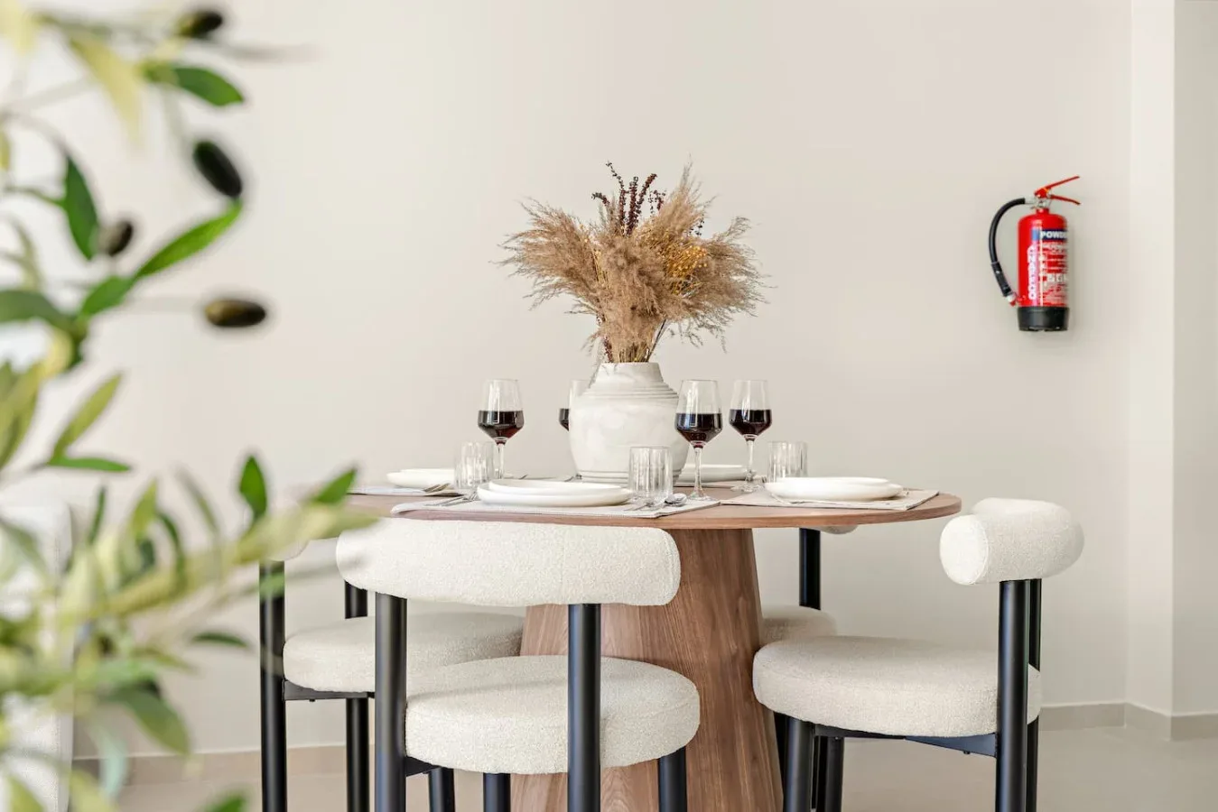 Un comedor con una mesa puesta, asientos tapizados y un jarrón con flores secas.