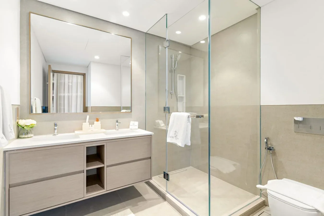 Un baño luminoso con lavabo, espejo grande y ducha de vidrio.