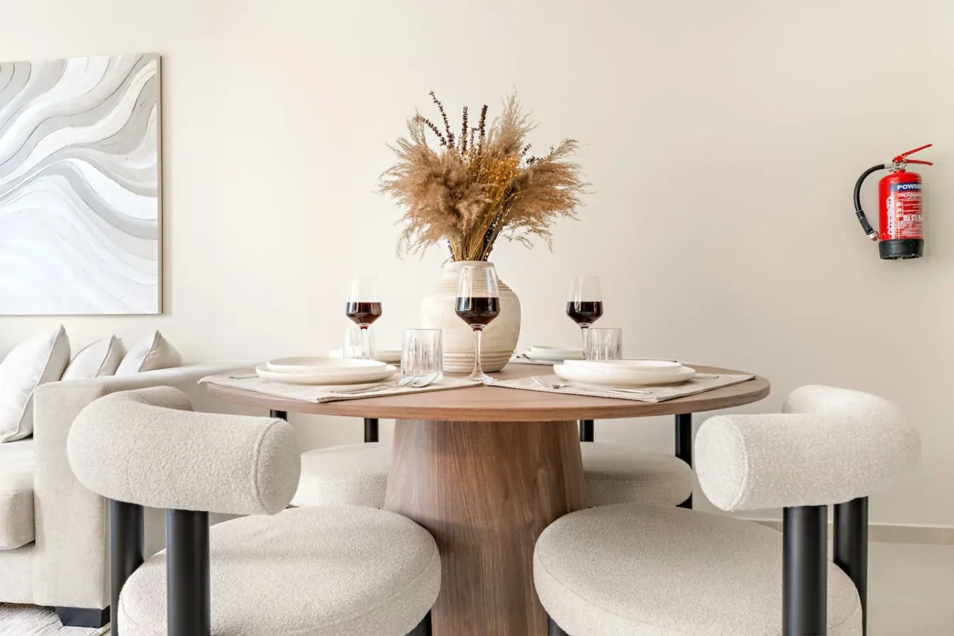 Comedor con una mesa redonda puesta con platos y un jarrón de flores secas.