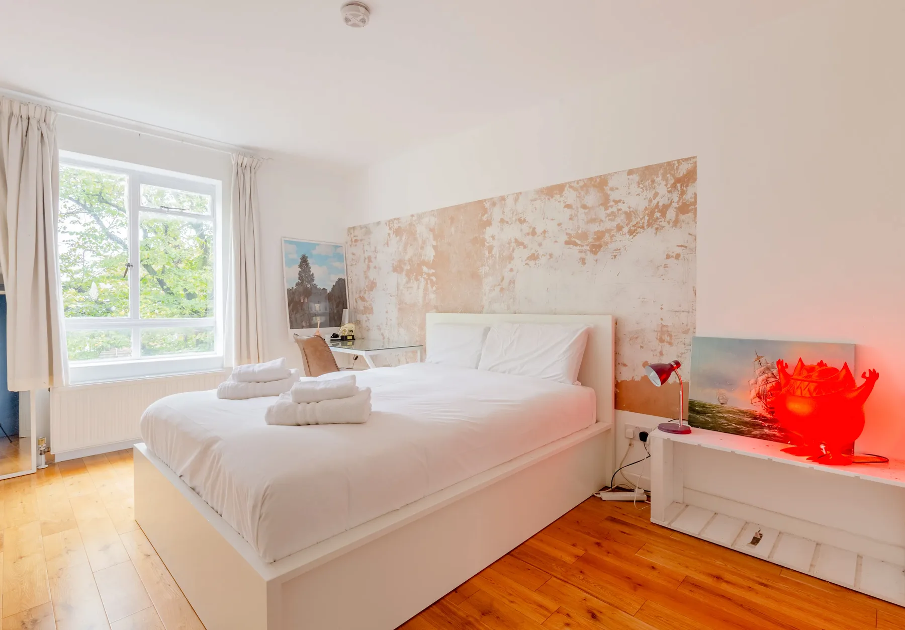 Un dormitorio luminoso con una cama blanca, una ventana grande y suelo de madera cálida.