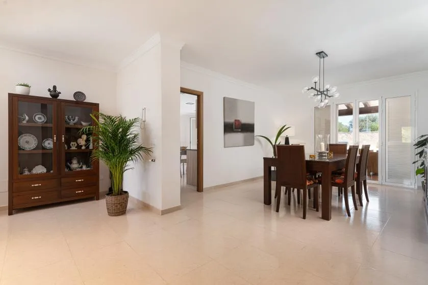 A bright dining area with a wooden table and display cabinet.
