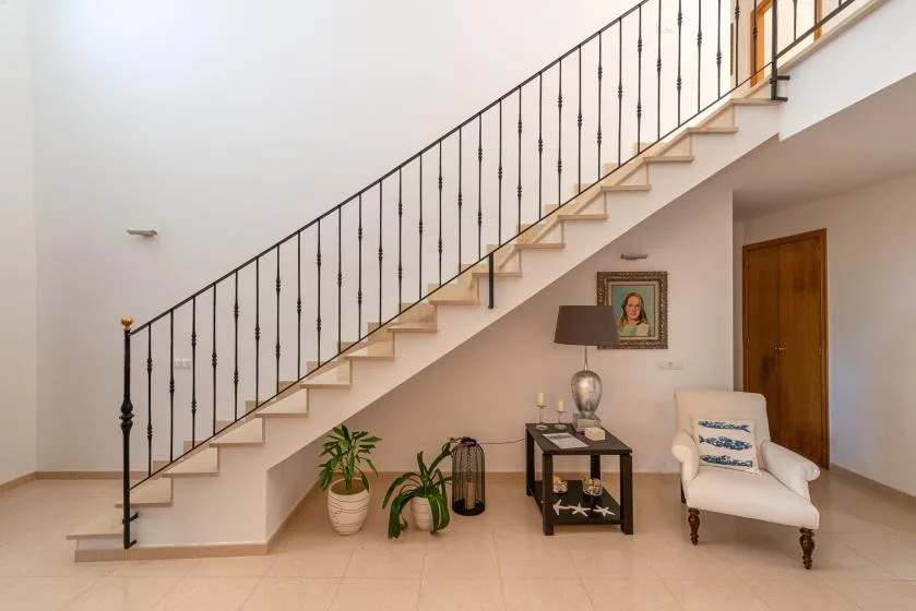 A staircase rises above a small seating area with a chair and console table.