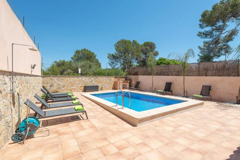 An outdoor swimming pool sits in a tiled courtyard with lounge seating.