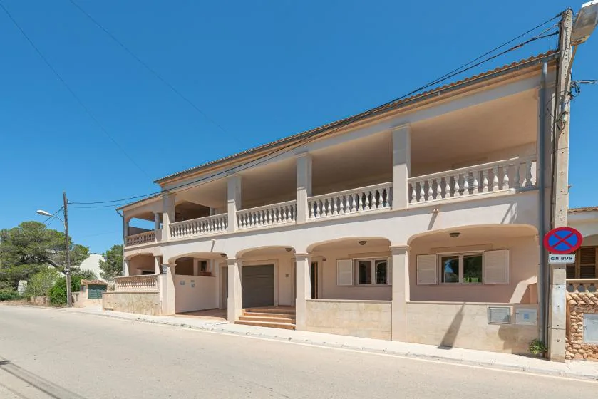 A multi-story building with a long balcony stands beside a quiet street.