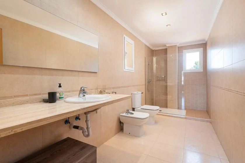 A tiled bathroom with a long sink counter and a glass shower area.