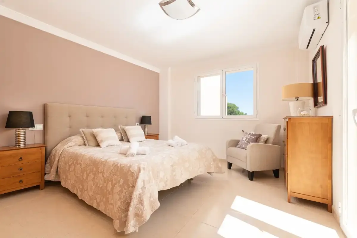 A bedroom with a double bed, bedside tables, and a chair beside the window.