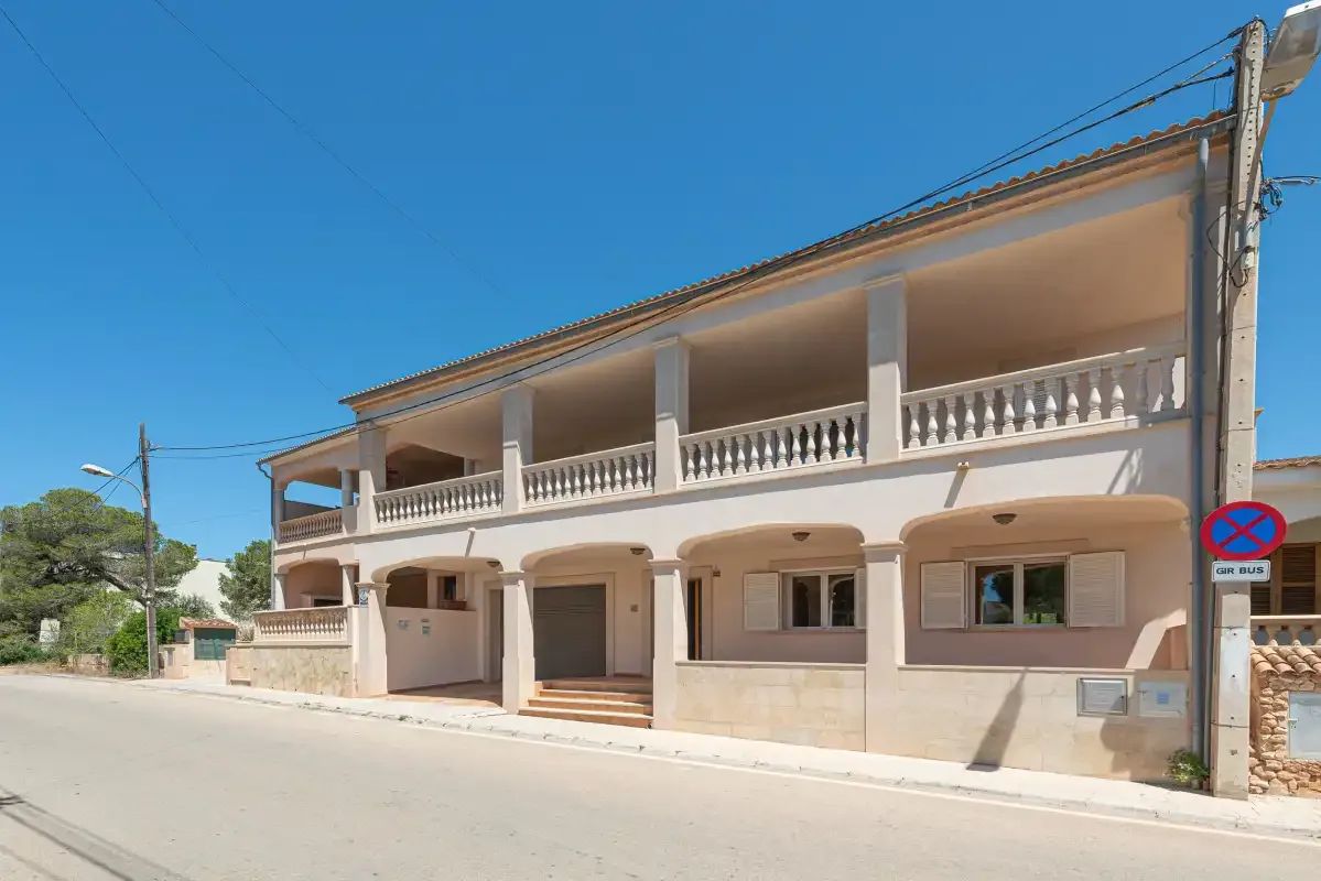 A two-story building with long balconies stands beside a sunny street.