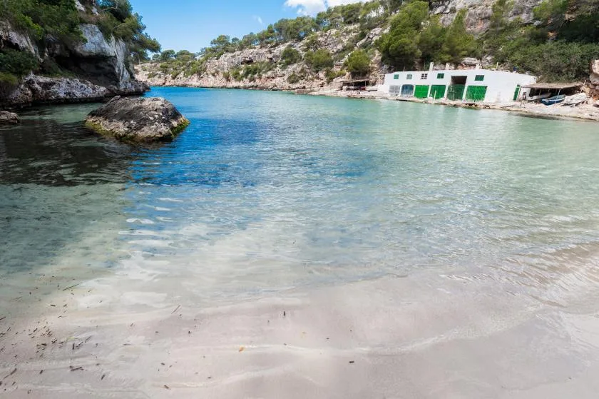 A clear inlet with rocky shores and a small white building beside the water.