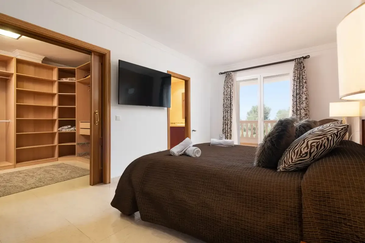 A bedroom with a bed, a television, and glass doors opening onto a balcony.