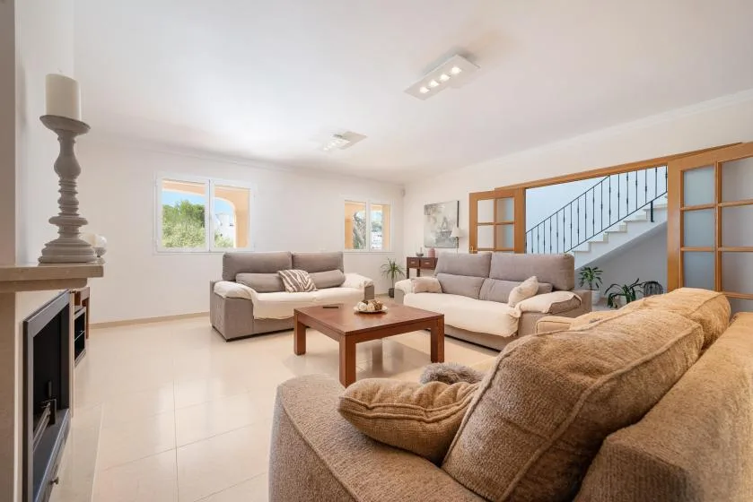 A bright living room with seating around a wooden coffee table and windows.