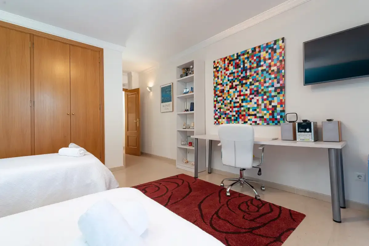 A bedroom with beds, a desk, and colorful wall art.