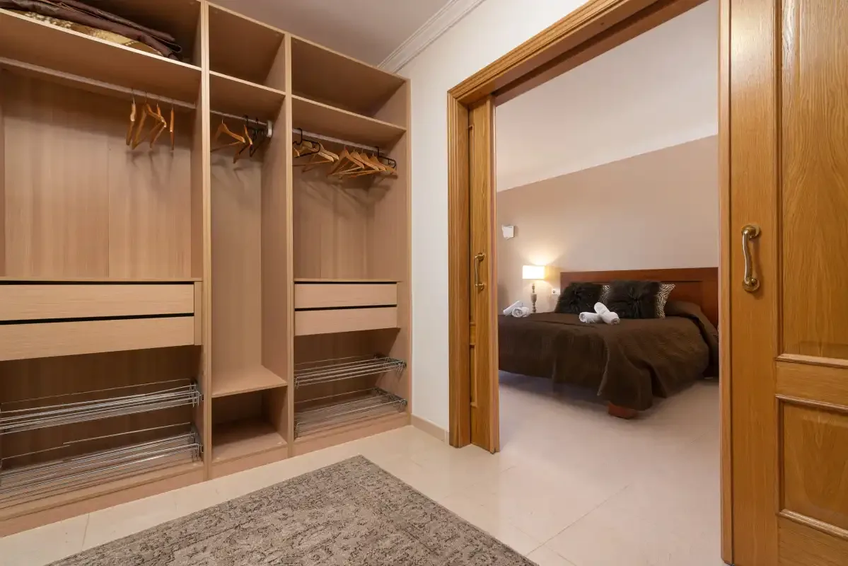 A walk-in closet opens onto a bedroom with a bed and bedside lamp.