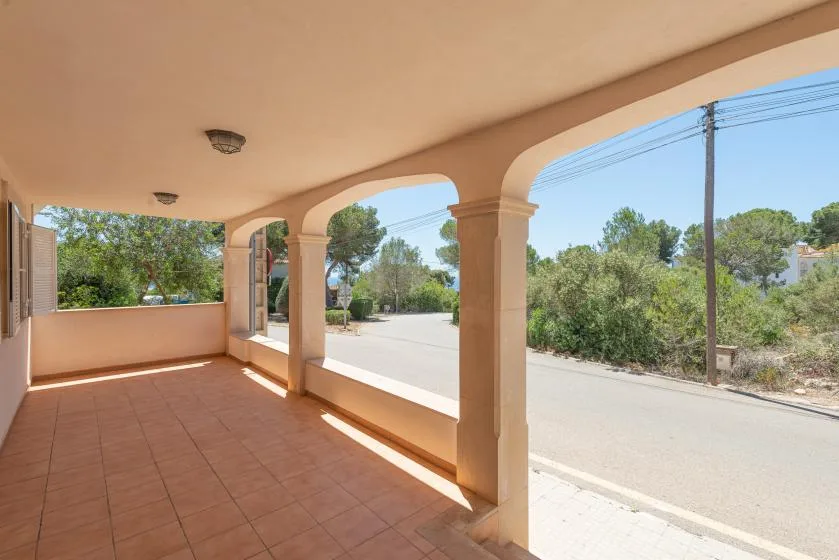 A covered outdoor terrace with tiled flooring and open arches overlooking a road.